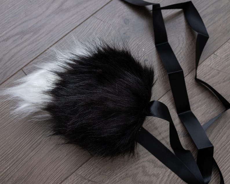 May include: A black and white faux fur tail with a black ribbon attached.