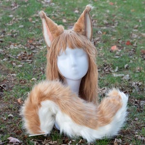 May include: A cosplay set featuring a wig with large, pointed ears and a matching tail. The ears and tail are a mix of brown, tan, and white faux fur. The wig has long, light brown hair. The set is displayed on a white mannequin head.
