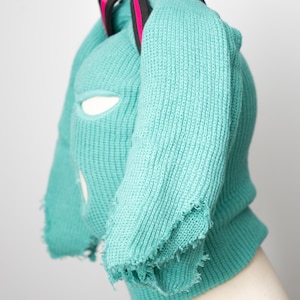 May include: A turquoise knitted balaclava with a frayed edge and a black strap with pink accents.