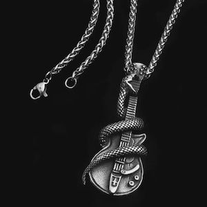 May include: A silver-coloured necklace with a pendant depicting an electric guitar wrapped by a snake. The guitar pendant has detailed fretwork and hardware. The necklace chain is a textured, linked design with a lobster clasp. The background is solid black.