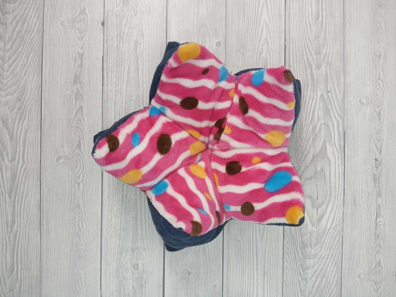 May include: A pink and white star-shaped pillow with brown and blue polka dots and stripes. The pillow is made of soft, plush fabric.