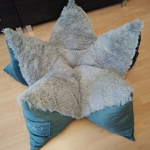May include: A star-shaped plush pet bed with a soft, gray, fuzzy exterior and a teal green interior. The bed is made of multiple pieces that are sewn together to form the star shape.