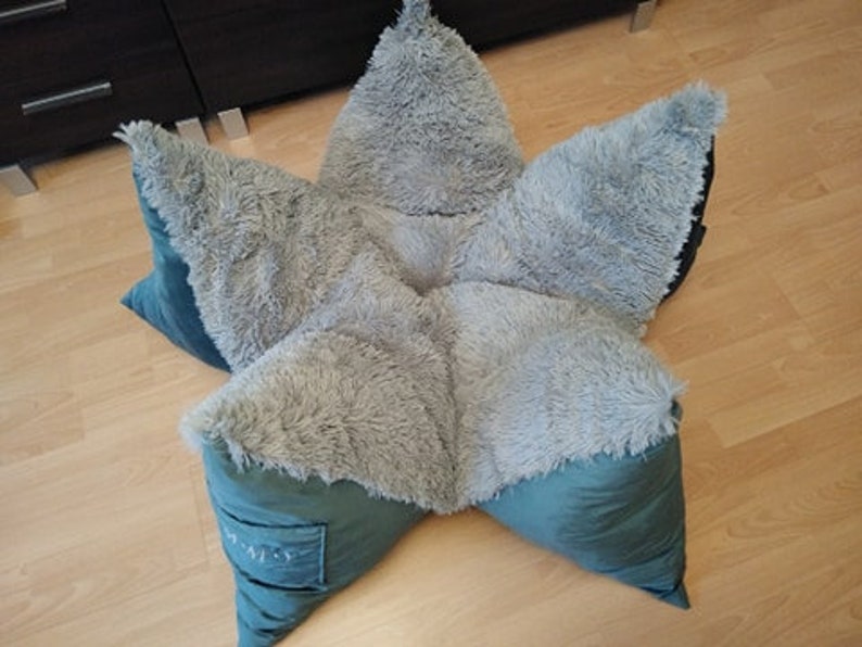 May include: A star-shaped plush pet bed with a soft, gray, fuzzy exterior and a teal green interior. The bed is made of multiple pieces that are sewn together to form the star shape.