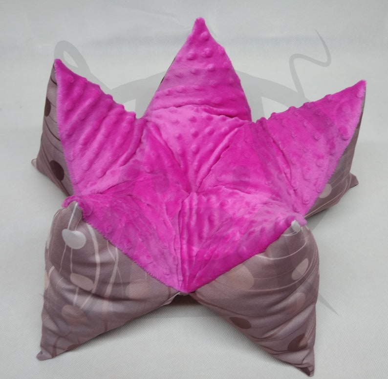 May include: A pink and brown star-shaped floor cushion with a soft, plush texture. The cushion is made of two different fabrics, one with a polka dot pattern and the other with a textured, fuzzy surface.