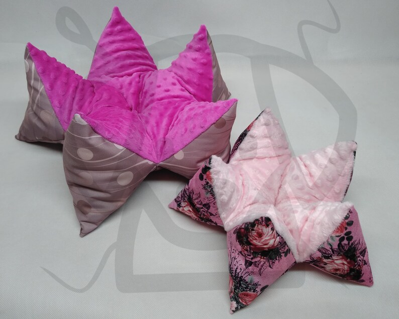 May include: Two pink star-shaped pillows with different patterns. The larger pillow has a pink and gray polka dot pattern, while the smaller pillow has a floral pattern.