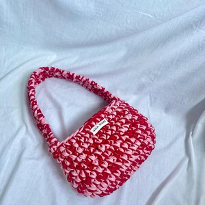 May include: A small pink and red crocheted handbag with a white label that says "little.monster".