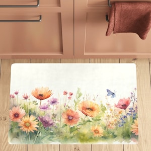 May include: A white kitchen mat with a watercolor design of a row of colorful flowers and a blue butterfly. The flowers are in shades of orange, yellow, pink, and purple.