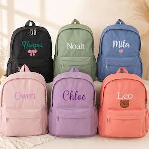 May include: Six backpacks in black, sage green, blue, light pink, lavender, and coral. Each bag features a front pocket, silver zippers, and a personalized name embroidered in the center, accompanied by small icons like a bow, tulip, or bear.