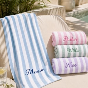 May include: A collection of four striped beach towels featuring embroidered names. One towel is blue and white with the name Maeve, while the others are stacked and feature pink with Parker, green with Willa, and purple with Nico embroidered on them.