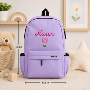 May include: A light purple backpack featuring the embroidered name Karen and a pink tulip graphic. The bag includes a front zippered pocket with a Mywa label, side pockets, and measures 15.8 inches in height and 11.8 inches in width.