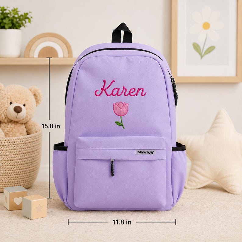 May include: A light purple backpack featuring the embroidered name Karen and a pink tulip graphic. The bag includes a front zippered pocket with a Mywa label, side pockets, and measures 15.8 inches in height and 11.8 inches in width.