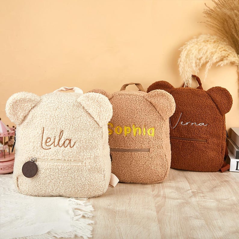 Pu&ograve; includere: Tre zaini a forma di orsetto in crema, beige e marrone. Ogni zaino ha una tasca con cerniera e il nome ricamato: Leila, Sophia e Verna. Gli zaini hanno dettagli a forma di orecchie e una maniglia superiore.