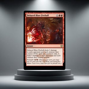 May include: A rectangular trading card titled Delayed Blast Fireball with a red border and a central illustration of a fiery explosion. The card text details game mechanics, including damage values and the foretell ability, set against a light background.