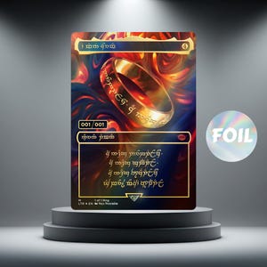 Könnte beinhalten: Sammelkarte mit einem goldenen Ring mit Inschriften, vor einem feurigen, abstrakten Hintergrund. Die Karte hat eine Folienoberfläche und wird auf einer mehrstufigen Plattform präsentiert. Der Text "FOIL" ist sichtbar.