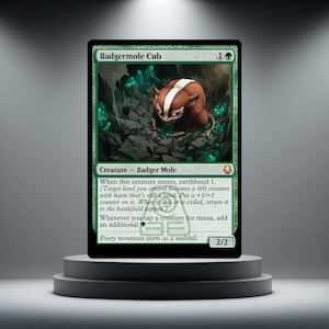 Puede incluir: Una carta coleccionable de Magic: The Gathering de color verde titulada Badgermole Cub. La carta muestra la ilustración de una criatura marrón y blanca similar a un tejón en una cueva rocosa oscura con cristales verdes brillantes.