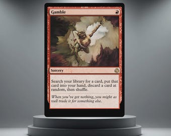 May include: A red Magic: The Gathering card labelled "Gamble." The card shows a creature in action against a cloudy backdrop. The text describes a sorcery spell. The card is displayed on a grey pedestal.