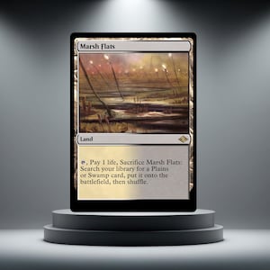 Peut inclure: Carte Magic: The Gathering "Marsh Flats" sur un piédestal gris. L'illustration montre un paysage de marais avec des plantes hautes et un ciel brumeux. Le type de carte est "Terrain", avec des instructions de jeu.