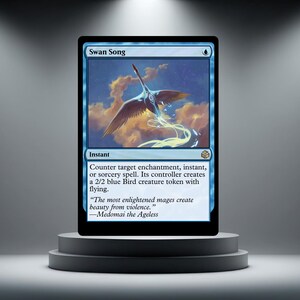 May include: A blue Magic: The Gathering card named "Swan Song" with a swan illustration. The card text details a spell that creates a 2/2 blue Bird creature token with flying. The card is displayed on a grey plinth.