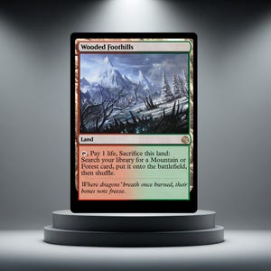 May include: A Magic: The Gathering card named "Wooded Foothills" showing a landscape of snow-covered mountains, bare trees, and a green and red border. The card text details land sacrifice for Mountain or Forest cards.