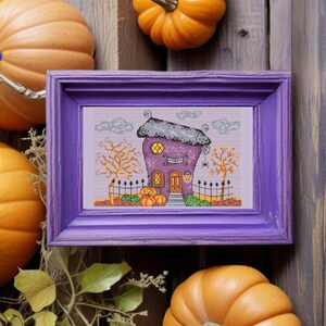 Puede incluir: Una casa de Halloween morada con un letrero que dice "Tarot" y una telaraña sobre la puerta. La casa está rodeada de calabazas y una valla. La imagen está enmarcada en un marco morado.
