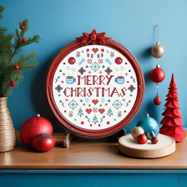 May include: A red framed embroidery hoop with a white background and a red and blue cross-stitch design that says "Merry Christmas". The design includes snowflakes, hearts, Christmas trees, and other festive elements.