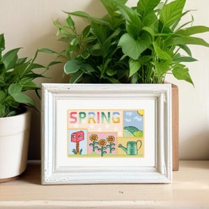 Puede incluir: Un marco blanco con un diseño de punto de cruz colorido que representa la primavera. El diseño incluye la palabra "SPRING" en letras de arcoíris, un buzón, girasoles y una regadera.