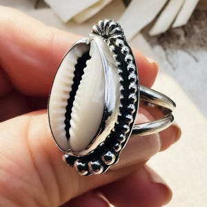 Silver ring with a shell design held in a hand against a neutral background