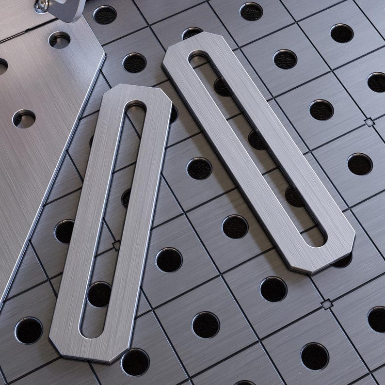 K&ouml;nnte beinhalten: Zwei silberne Metallstreifen mit rechteckiger Form und einer langen, schmalen &Ouml;ffnung in der Mitte. Die Streifen liegen auf einer grauen Metalloberfl&auml;che mit einem Lochraster.