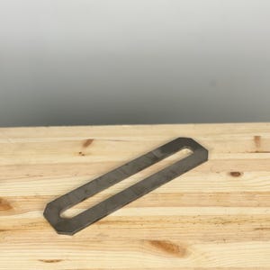 K&ouml;nnte beinhalten: Eine U-f&ouml;rmige Metallhalterung mit einem langen Schlitz in der Mitte. Die Halterung ist aus silberfarbenem Metall und liegt auf einer hellbraunen Holzoberfl&auml;che.