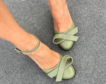 Op de afbeelding: Een paar sagegroene leren hakken met een strikdetail op de neus. De schoenen hebben enkelbandjes met gespen.