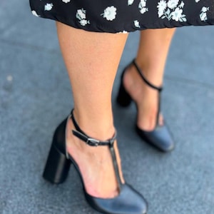May include: A pair of black heeled shoes with a t-strap design. The shoes have a chunky heel and a pointed toe.