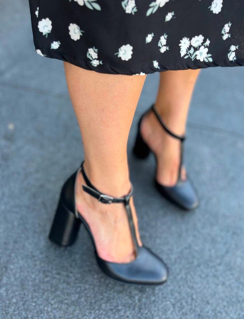 May include: A pair of black heeled shoes with a t-strap design. The shoes have a chunky heel and a pointed toe.