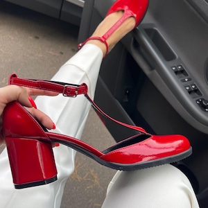 May include: Red patent leather heeled shoes with a T-strap and a chunky block heel.