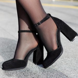 May include: Black suede ankle strap heels with a chunky block heel. The heels have a closed toe and an open back.