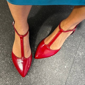May include: A pair of red patent leather heeled shoes with a T-strap design.