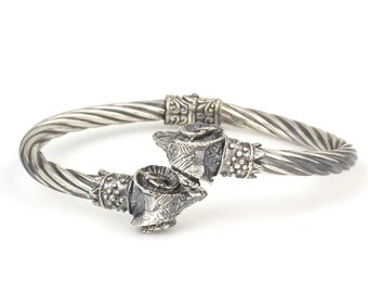May include: A silver bangle bracelet with a twisted design and two decorative animal head accents.