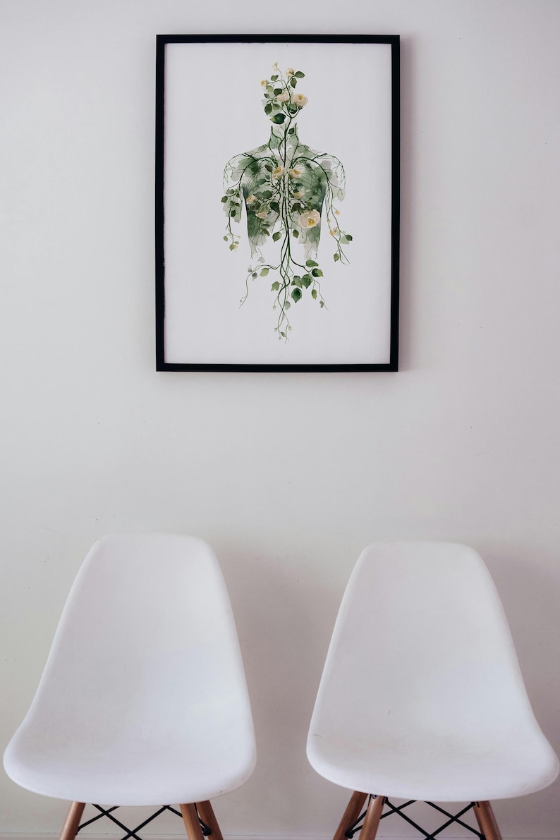 May include: A framed art print depicting a human form with botanical elements. The artwork features a black frame and a white background. The human form is illustrated with green veins and adorned with yellow flowers and green leaves. Two white chairs are in the foreground.