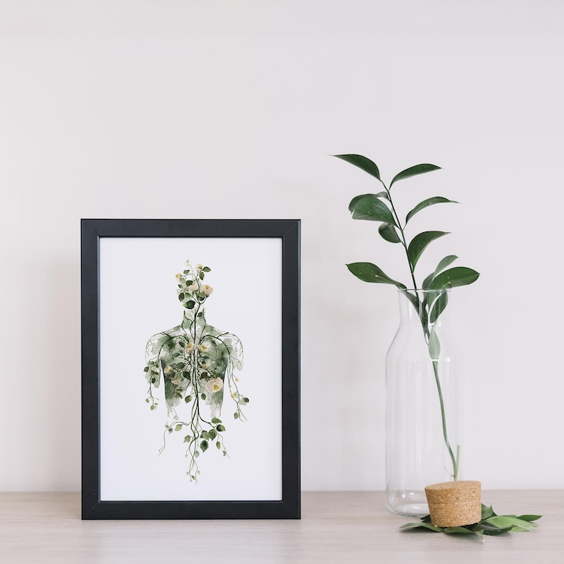 May include: A framed art print featuring a botanical illustration of a human form composed of delicate flowers and vines. The artwork is set against a white background and framed in a black frame. A clear glass vase with a green plant and a cork stopper are next to the frame.