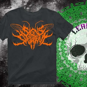 May include: Dark gray t-shirt with an orange graphic design featuring insect wings and stylized text. The image also includes a skull with the word "LEAFIOH" and a green and white patterned background.