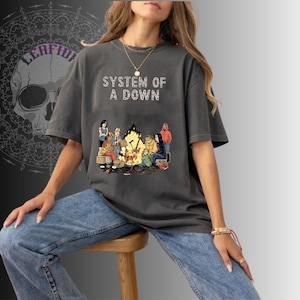 Puede incluir: Camiseta gris oscuro con el texto blanco "SYSTEM OF A DOWN". La camiseta presenta un gráfico de personas alrededor de una fogata. La camiseta es de estilo casual y unisex.