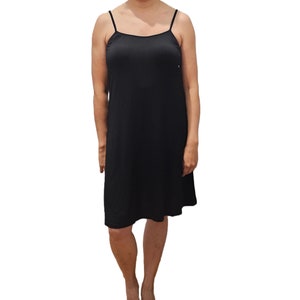 Pode incluir: Um vestido preto com finas alças espaguete. O vestido tem comprimento até ao joelho e é feito de um tecido liso e sólido. O decote é simples e a saia é ligeiramente rodada.