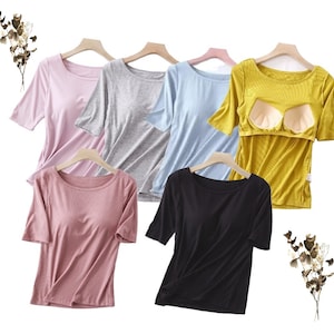 Puede incluir: Cinco camisas de manga corta en diferentes colores, incluyendo rosa, gris, azul, amarillo y negro. Las camisas tienen un cuello redondo y están hechas de un tejido de canalé.