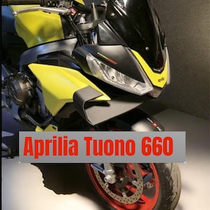 Puede incluir: Una motocicleta Aprilia Tuono 660 amarilla y negra. La moto tiene un parabrisas negro, ruedas rojas y un diseño elegante. El texto "Aprilia Tuono 660" se muestra en rojo sobre un fondo gris.