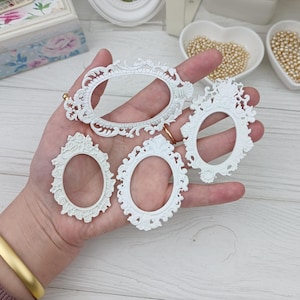 Peut inclure: Quatre cadres photo ovales blancs ornés, avec des détails de volutes et des accents floraux. Les cadres varient en taille et en design, avec des centres ouverts. Les cadres sont présentés sur un fond clair, suggérant un projet artisanal ou de bricolage.