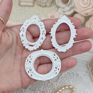 May include: Three small white decorative frames with intricate scrollwork and floral relief details. The set includes two oval-shaped frames and one circular frame, all featuring ornate borders and a matte finish, suitable for craft projects.