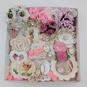 May include: A box overflowing with craft supplies in pink, cream, and white. It contains fabric flowers, crochet pieces, lace, vintage images, and decorative embellishments. Ideal for crafting and scrapbooking, the contents offer a vintage aesthetic.
