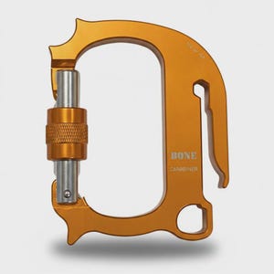 Peut inclure: Un mousqueton en métal orange avec un doigt de verrouillage argenté et une bague filetée texturée. Le cadre porte l'inscription BONE CARABINER et la gravure 150 of 150. Il présente une forme en D avec un crochet latéral et un petit trou circulaire.