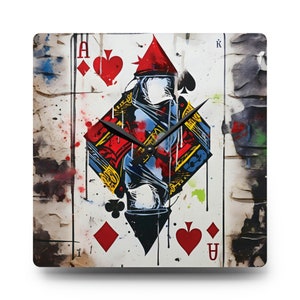May include: A square clock with a white background and a black, red, and blue design of the Ace of Spades playing card. The clock hands are black and the clock face is a grunge-style design.