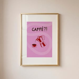 May include: Framed art print featuring a pink background with the word "CAFFÉ?!" in brown. A red illustration of a coffee maker pouring coffee into a cup is below the text. The print is in a gold frame.