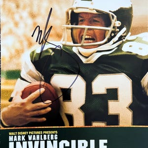 May include: A movie poster for the film "Invincible" starring Mark Wahlberg. The poster features a close-up of Wahlberg as a football player wearing a green and white uniform. The text "Invincible" is in large, bold letters and the text "Now Playing" is below it.